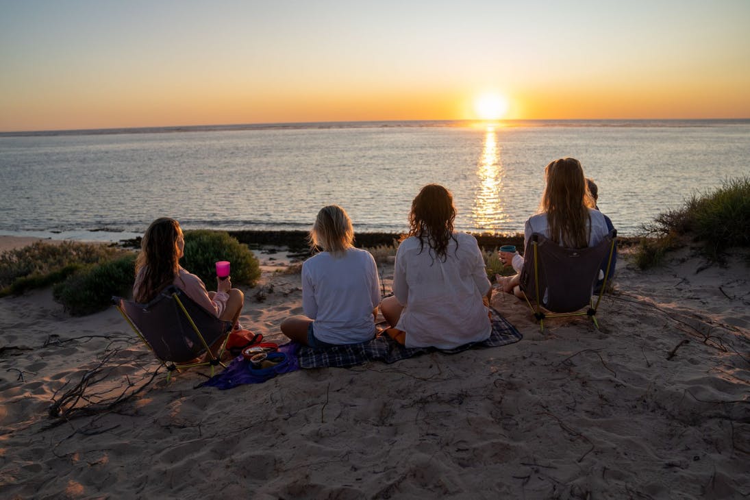Group of friends sitting and eating on a Ningaloo beach at sunset